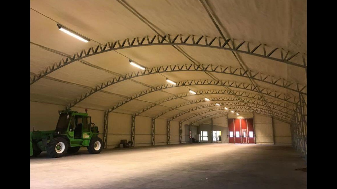 Sienu siltināšana no iekšpuses: Liels angārs ar siltinātām sienām. Angārā ir zaļš traktors.